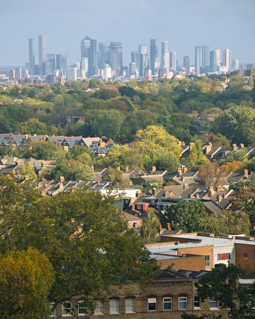 A panoramic view of a lush green residential garden with well-maintained lawns, a variety of mature deciduous trees displaying vibrant autumn foliage, and neatly trimmed hedges. The garden features a
